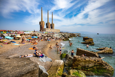Personas bañándose en la playa con las tres chimeneas al fondo